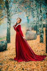 Obraz na płótnie Canvas Portrait of magnificent Fashion gothic girl standing in autumn forest .Fantasy art work.Amazing red haired model in claret dress with a sword .Fairytale about young princess-warrior. 