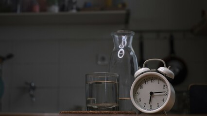 Alarm clock, a glass and a bottle of water on dark background, conceptual photo, reminder to drink...