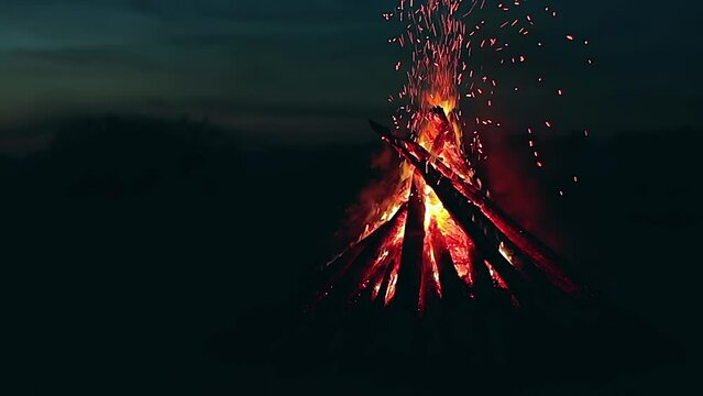 Big Burning Campfire at Summer Night against the Blue Sky. Wood on Fire. Flying Sparks. Travel and Tourism Concept. Giant Flaming Bonfire - Static Shot, Slow Motion