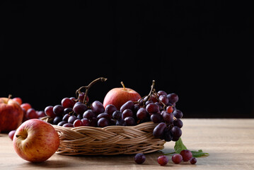 Red grape and apple fruit on wooden table with black background