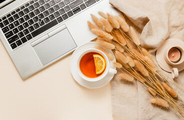 Tea with lemon, laptop, candle, lagurus grass on linen cloth, aesthetic home workplace, cozy feminine office desk. Bohemian style, autumn and winter theme