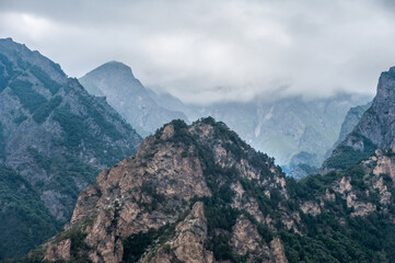 Fototapeta premium Mountain peaks with trees against a background of cloudy sky and clouds
