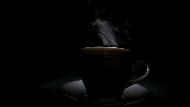 Silhouette of a mug with a warm drink and a fancy curly steam rising up. A steaming coffee cup on a black background. Morning coffee.