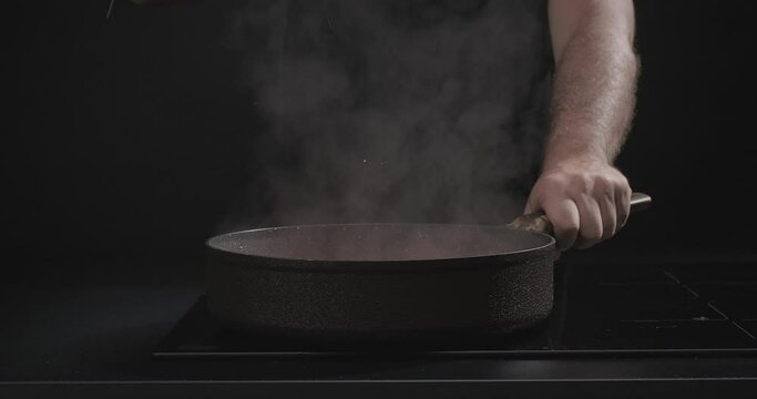 Male hand opening a glass lid and hot steam coming out of a boiling pan, isolated on a black background. Slow motion