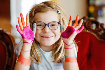 Little preschool girl painting with felt pens on hands. Creative cute child showing hands and arms...