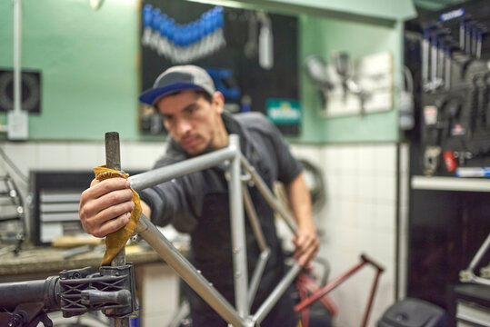 Hispanic man preparing a bicycle frame to paint in his bike workshop. Selective focus on the worker right hand.