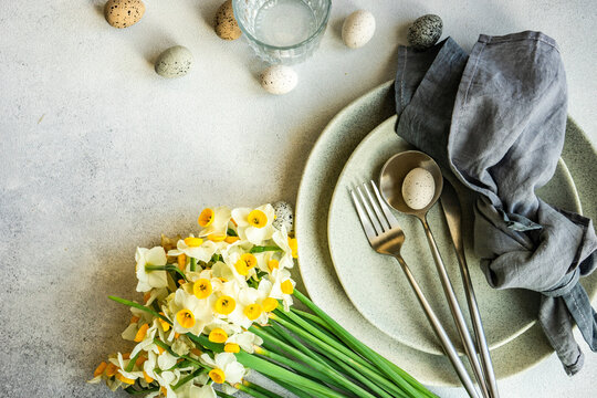 Place setting for Easter festive dinner with daffodil flowers and eggs on concrete background