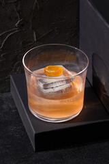 A rich whiskey cocktail infused with caramel notes, gracefully served in a rocks glass on an elevated platform, exuding minimalist bar elegance against a deep black setting