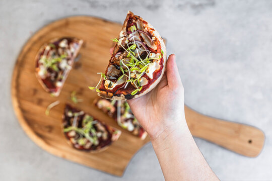 Hand Holding A Slice Of Vegetarian Pizza With Mushrooms And Sprouts