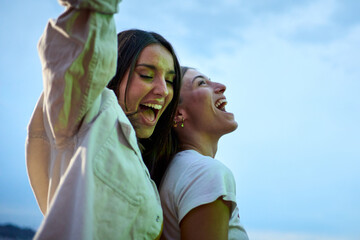 Two excited young Caucasian friends hanging out dancing party in evening having fun at weekend. Happy beautiful people enjoying leisure time outdoor. Attractive gen z women celebrating summer night.