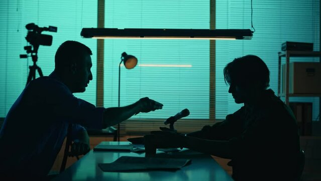 Medium silhouette video of a offender, perpetrator or prisoner sitting in the room. The detective brings him a cup of water and begins the interrogation process.