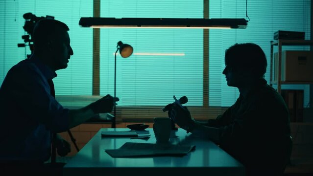 Medium silhouette video of a offender, perpetrator or prisoner sitting in the room. The detective brings him a cup of water and begins the interrogation process.