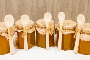 A small yellow jar of honey with a decorative lid made of beige paper and a bow, a small wooden...
