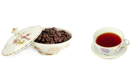 Obraz na płótnie Canvas Tea in a porcelain cup and chocolate dragee in a vintage candy bowl isolated on a white. Wide photo. Free space for text. Collage.