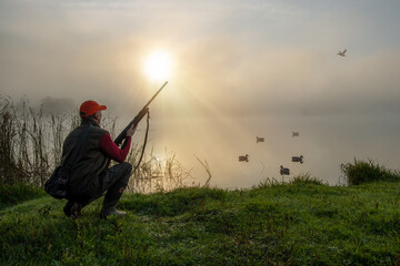 Duck Hunter. Waterfowl hunter sitting at riverside during duck hunting at sunrise.