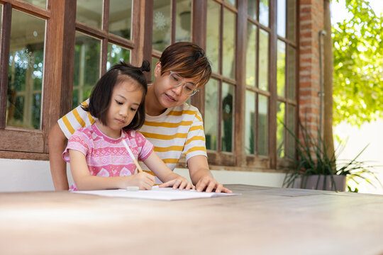Asian mother, her adorable daughter, are seated together at an outdoor table, for close-up learning session which supervise and explains concepts for child's joyful and effective learning experience.