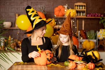 halloween, mom and daughter child in a witch costume with pumpkins and a big spider in a dark kitchen decorates a pumpkin during the Halloween celebration