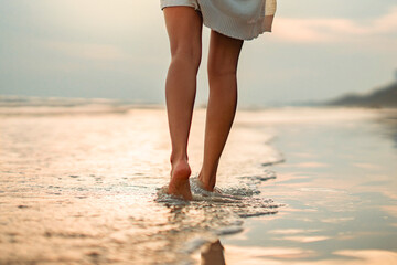 Closeup of woman feet walking on sand beach during a golden hour sunset. Travel and relaxing in...