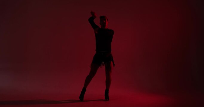 The striking silhouette of a man showcases his voguing dance style against a red backdrop. His expressive and dynamic movements create a visually captivating and artistically engaging performance.
