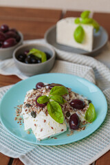 Feta cheese sliced on blue plate with sesame, flax seeds, served with black olives and basil leaves. Delicious and healthy breakfast on terrace