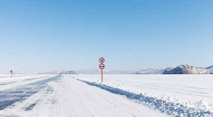Baikal Lake in sunny winter day. View of ice road to Olkhon Island with road signs. Extreme driving on ice crossing over frozen Small Sea at cold February day. Winter travel and adventure concept