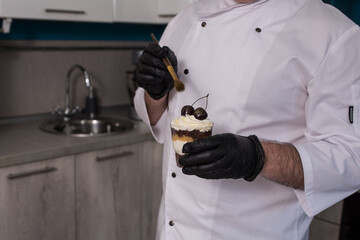 Close-up of a male pastry chef decorating a dessert in the kitchen, a male chef preparing a trifle in a glass cup