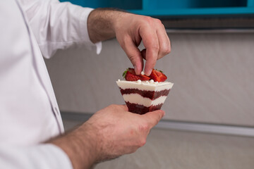 Close-up of a male pastry chef decorating a dessert in the kitchen, a male chef preparing a trifle in a glass cup