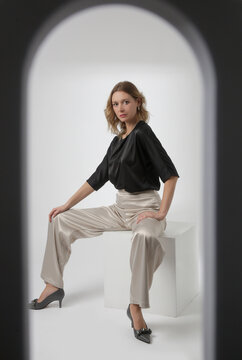Serie of studio photos of young female model wearing simple beautiful outfit, silk satin black blouse and white wide leg trousers