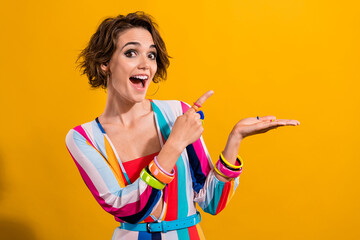Photo of funny omg joking girl pointing finger palm demonstrating crazy offer indicating astonished isolated on yellow color background