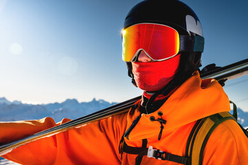 Portrait of a skier with skis on his shoulder. Guy on a background of a mountain range on a sunny...