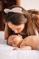 Mom kissing her baby in diaper sleeps placidly in bed