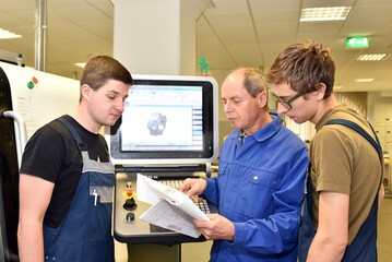 young apprentices in technical vocational training are taught by older trainers on a cnc lathes machine - 650270831