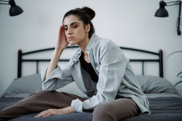 Tired and frustrated brunette woman sitting on blurred bed at home, burnout concept