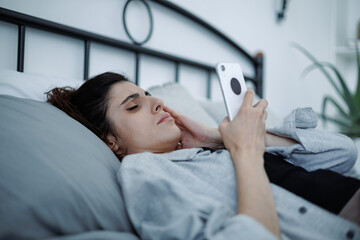 Woman with smartphone suffering from emotional stress and depression on bed at home