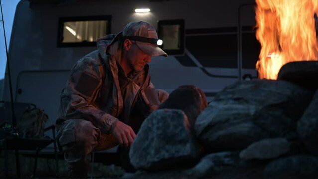 Hunter Wearing Camouflage Coating Burning Campfire Next to His Motorhome Camper Van RV