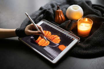 Girl's hand in special glove draws still life picture with pumkins on electronic tablet near...