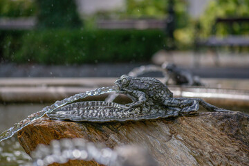 Fountain element in the form of a metal frog pouring a stream of water from its mouth