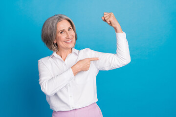 Photo of cheerful positive woman dressed white shirt pointing finger arm biceps isolated blue color...