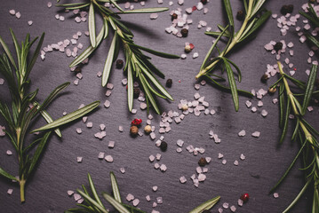 close-up of rosemary plant on black serving board with pepper and salt