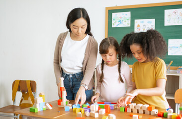 Multi-ethnic group of children school standing and playing with colorful blocks on table with Female Asian teacher in classroom. Education brain training development for children skill concept.