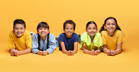 Lovely diverse kids lying on floor on yellow background