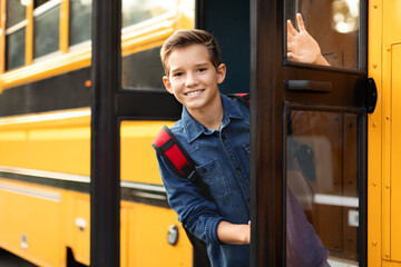 Preteen boy standing in door of school bus and looking at camera