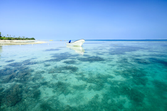 White Little Boat on Crystal Clear Calm Waters with the Island in the Background