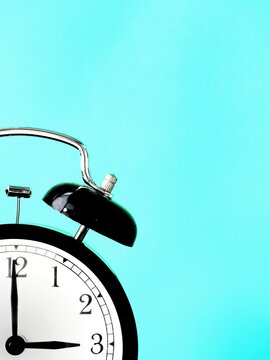 Black retro alarm clock at 3 three o clock on a blue background with copy space to add text 3am 3pm