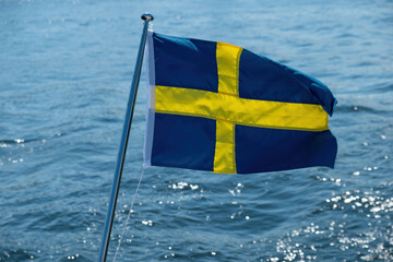 Sweden national flag waving on boat flagpole, blur sea water background,