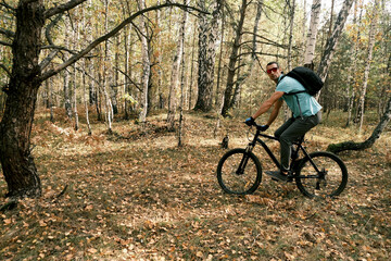 Fototapeta na wymiar Travel by bike.A man with a backpack and gloves rides a mountain bike through the forest in autumn.An active lifestyle.Mountain Bike