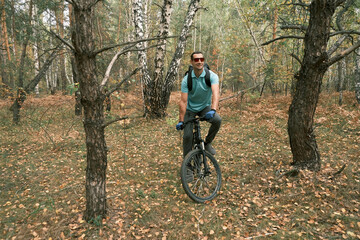 Fototapeta na wymiar man with a backpack and gloves rides a mountain bike through the forest in autumn.An active lifestyle.Mountain Bike