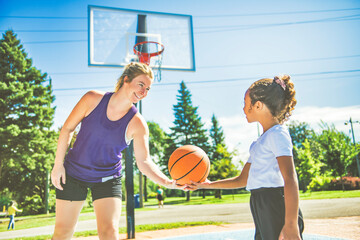 Mother and little daughter play basketball outside