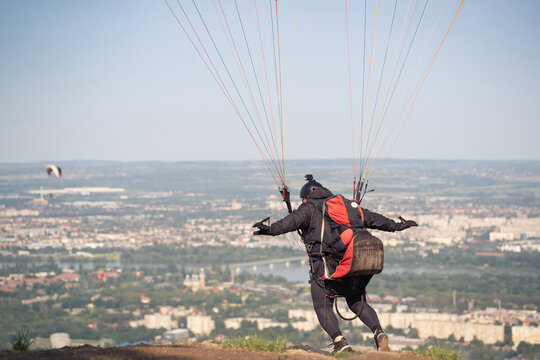 A paraglider is about to run to catch the wind and join the others in the air. Cityscape in the background.