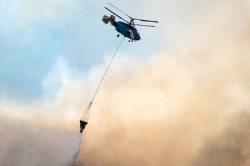 Helicóptero a descarregar a água do balde sobre um incêndio florestal que deixa muito fumo no ar